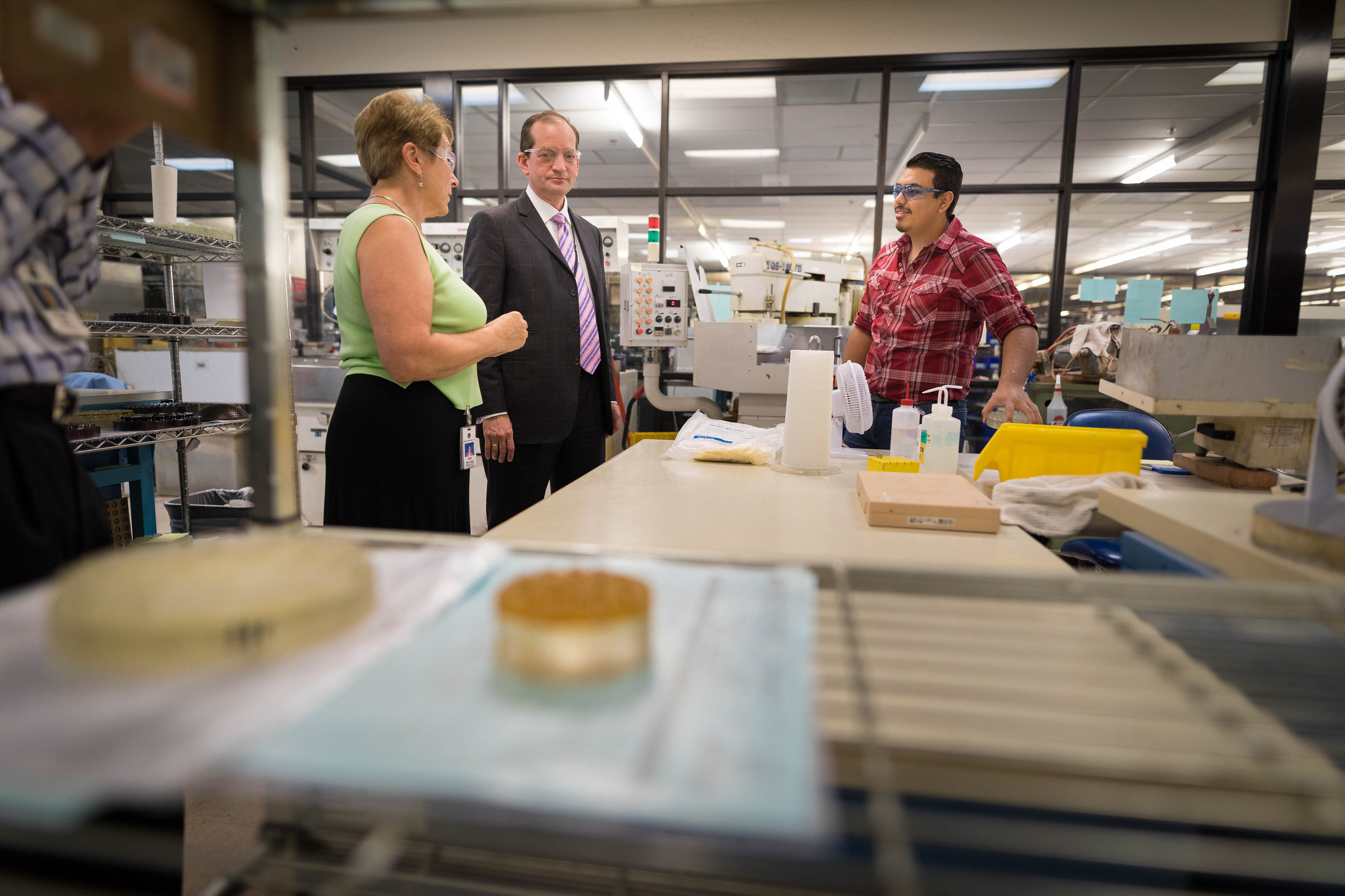 Three people in conversation inside a laboratory setting with various equipment and materials on tables.