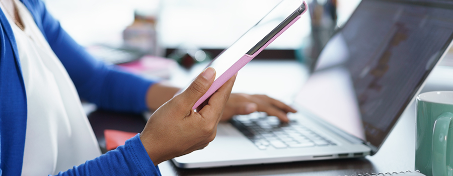Person holding a tablet in front of a laptop, with a green mug nearby on a desk.