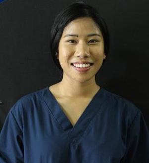 Person wearing a dark blue scrub top, smiling in front of a black background.