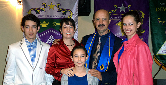 A family of five poses together, dressed in formal attire with a banner behind them displaying