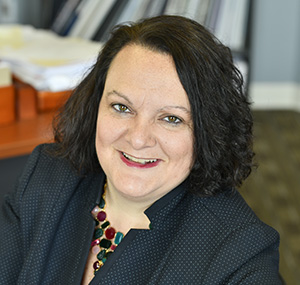 A person with dark hair and a black jacket smiles at the camera.