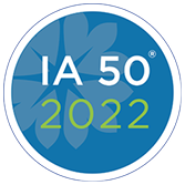 Circular logo with "IA 50 2022" text in white and green on a blue background with a subtle leaf pattern.