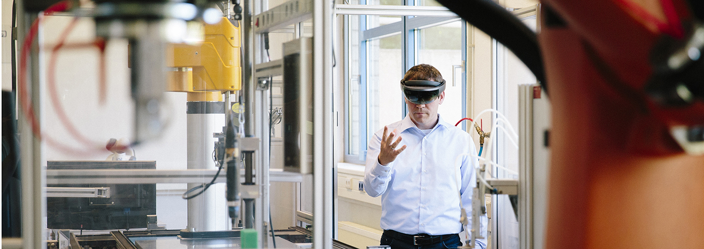 A person in a white shirt wearing augmented reality glasses interacts with machinery in a lab setting.