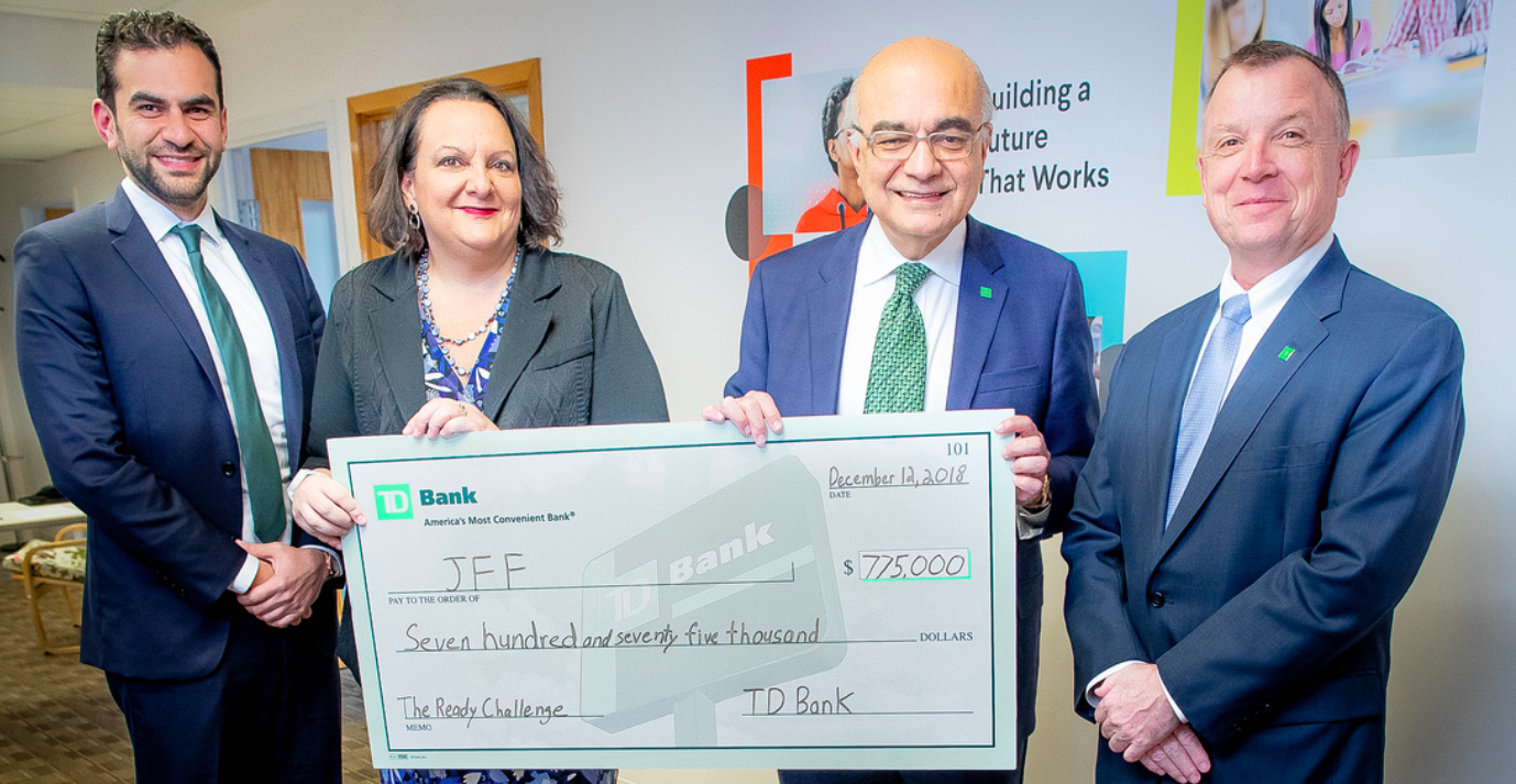 Four people are standing and smiling, holding a large check for $775,000.