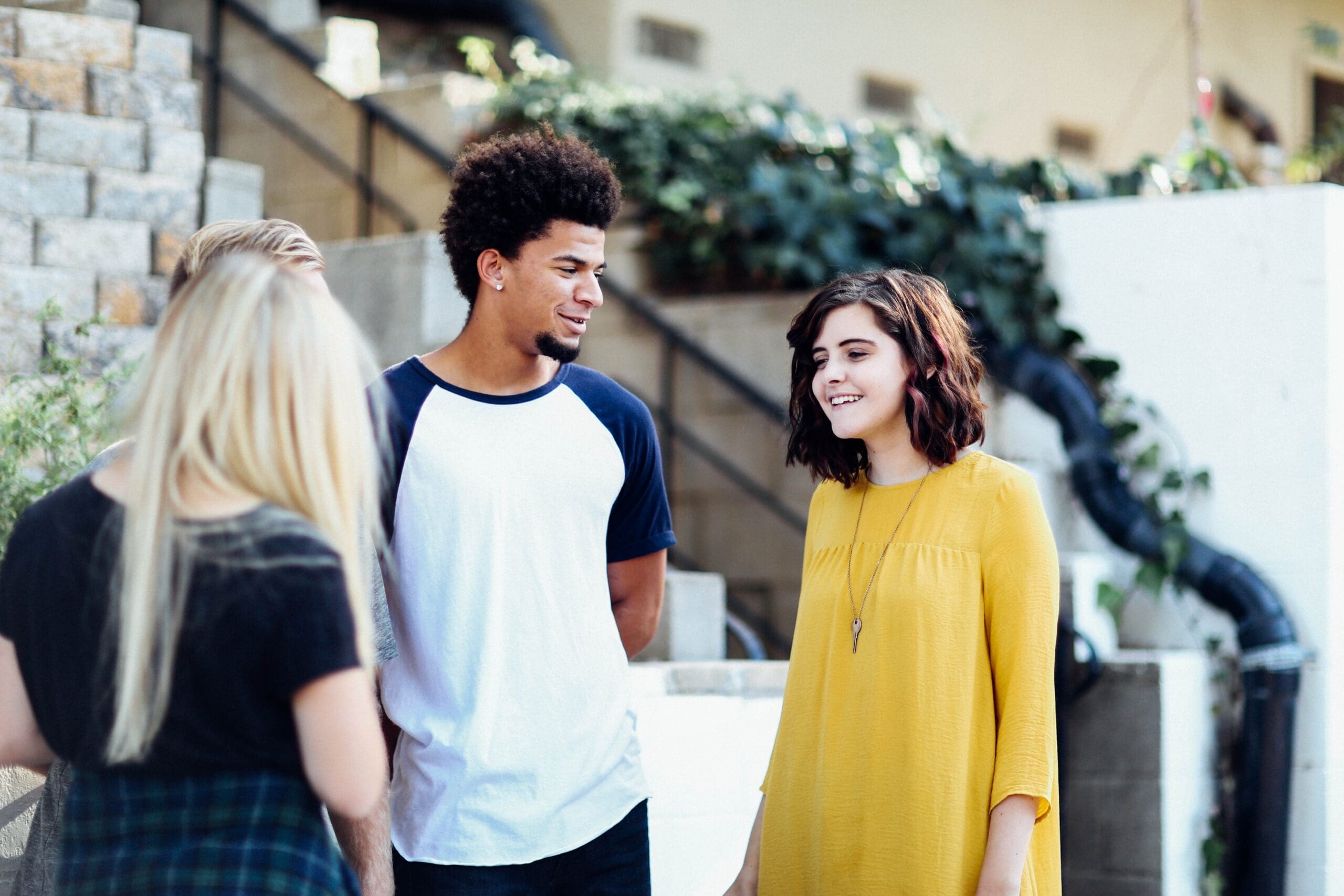 Four people talking and smiling outside near stone steps and greenery.
