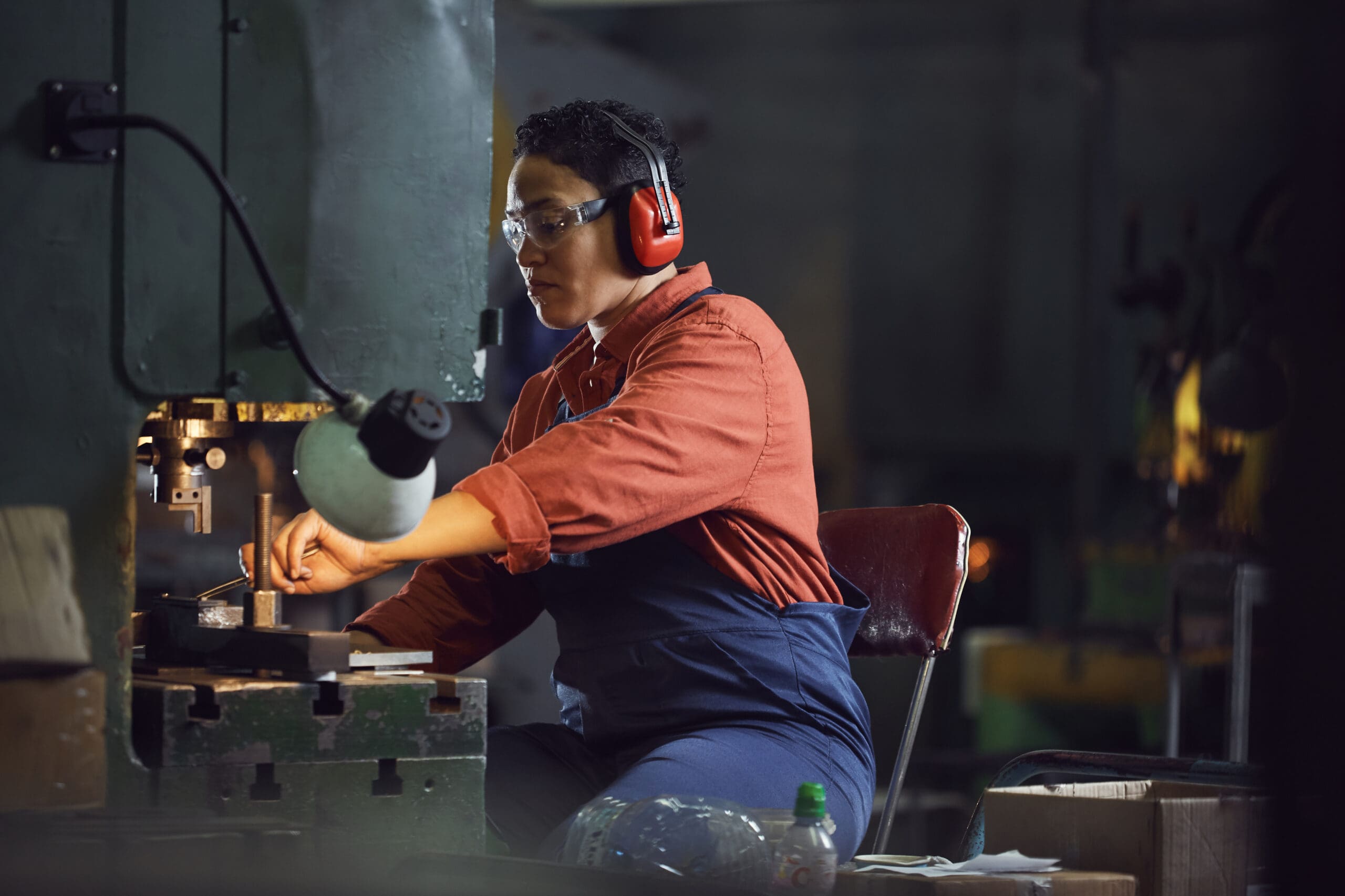 Person wearing safety gear operates industrial machinery in a workshop setting.