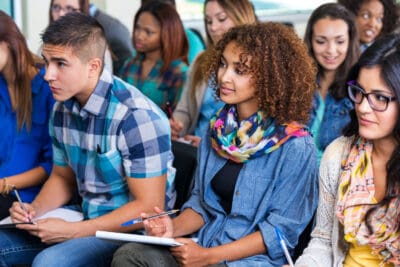A group of students sitting in a classroom, attentively listening and taking notes.