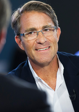 A person wearing glasses and a suit is smiling during a conversation.