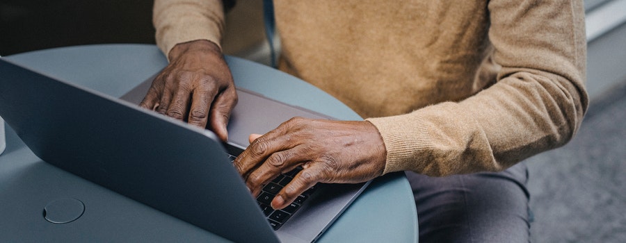 Person in a beige sweater typing on a laptop at a round table.