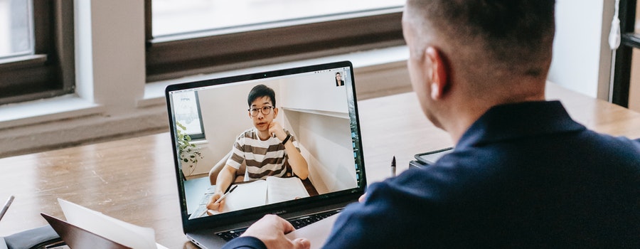 A person sits at a desk during a video call with another person on a laptop screen.