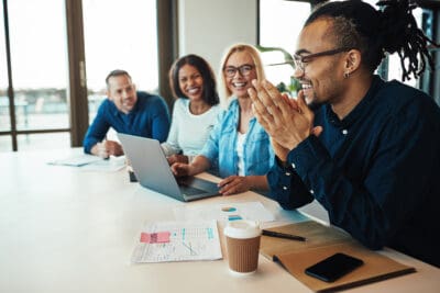 Young African American office worker laughing while sitting with a group of diverse colleagues during a meeting