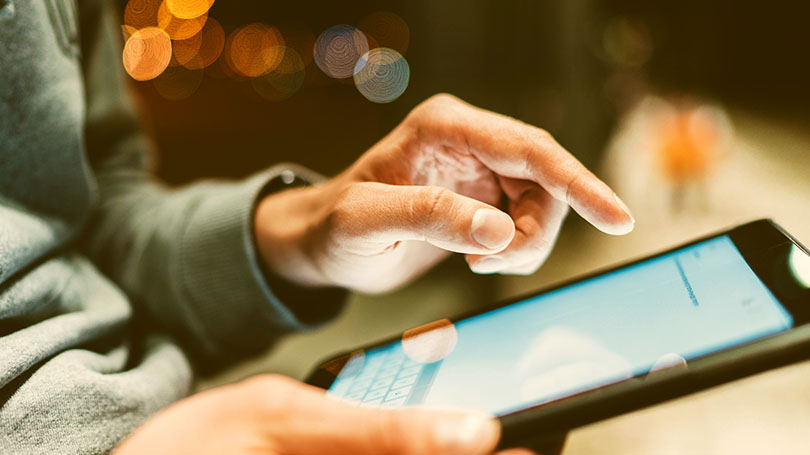 A person uses a smartphone, touching the screen with one hand. The background is blurred with circular lights.