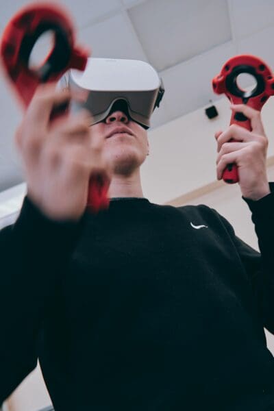 Person wearing a virtual reality headset holds two controllers in a room with a ceiling light.