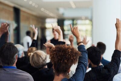A group of people seated indoors raise their hands, actively participating in a meeting focused on workforce development.