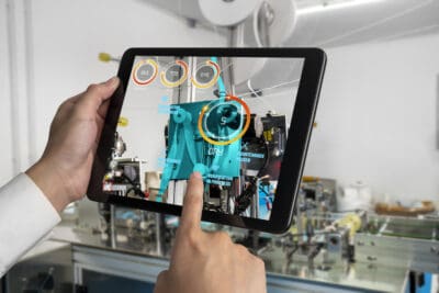 Person using a tablet to monitor machinery with augmented reality in a factory setting.