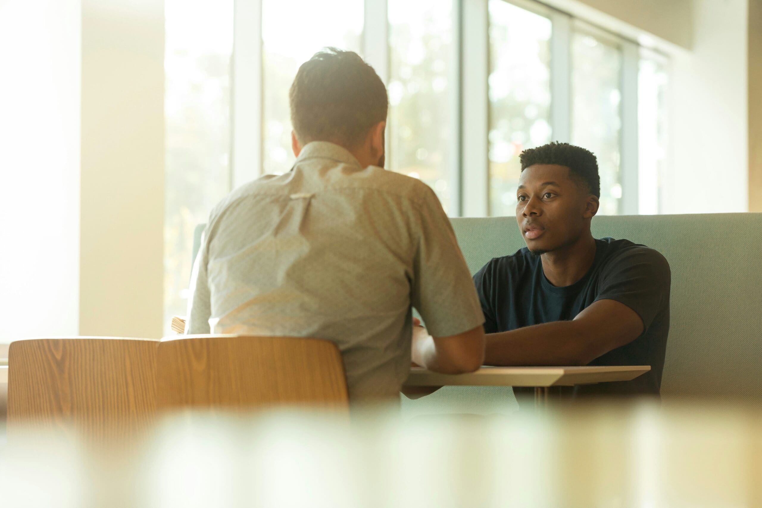 Two people are seated at a table in a well-lit setting, engaged in conversation.