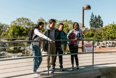 Four people standing by a railing outdoors, discussing dual enrollment opportunities, with trees and a lamp post in the background.