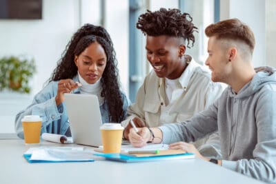 Multiracial group of college students wearing casual studying together, discussing and using laptop.