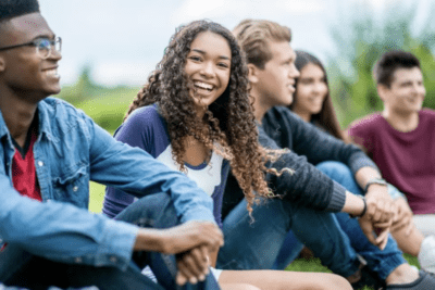 A group of young people sitting on grass, smiling outdoors.