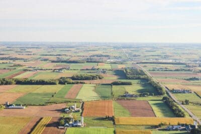 Aerial view of a vast rural landscape with a patchwork of fields, roads, and scattered buildings under a clear sky.