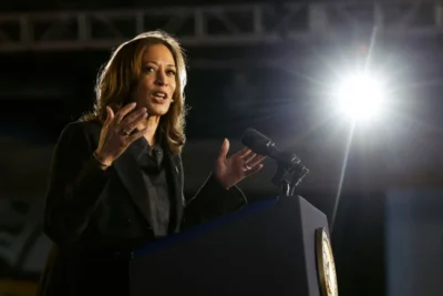 Kamala Harris is speaking at a podium with a microphone. A bright spotlight shines behind her.