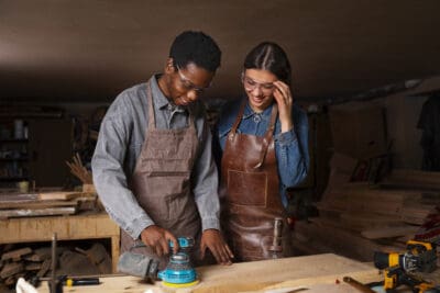 Two smiling people working in a wood workshop.