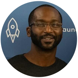 A person with glasses and a beard is smiling in front of a blue background with a rocket design.