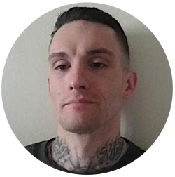 Man with short dark hair and neck tattoos against a plain background.