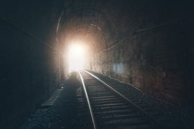 Railway tracks inside a dark tunnel lead to a bright light at the end.
