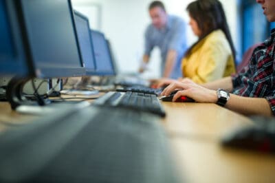 People working at computers in an office setting, with a focus on keyboards in the foreground.
