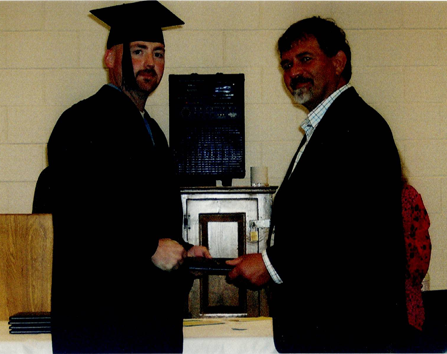 Graduate in cap and gown receives diploma from a man in a suit during a ceremony.