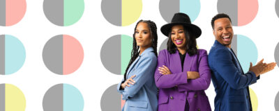 Three people stand smiling against a colorful geometric background, dressed in pastel suits.