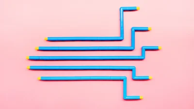 Four parallel blue plastic pipes with yellow ends are arranged in a staggered, zigzag pattern on a pink background.