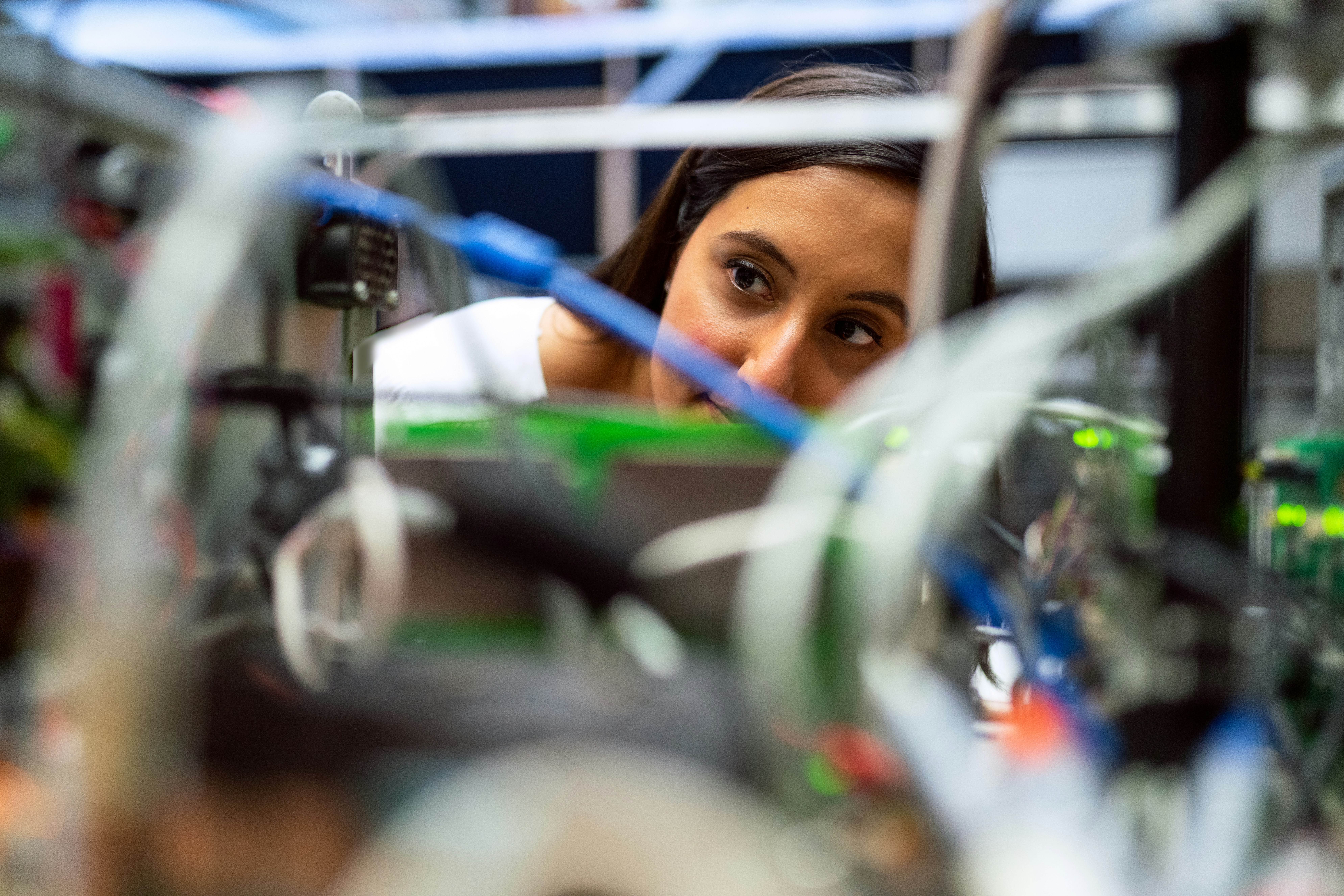 A woman closely examines electronic components and wires in a technical or laboratory setting.