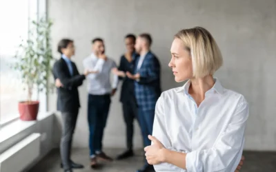 A woman in a white shirt stands in the foreground with arms crossed, looking away from a group of four men in business attire talking in the background.