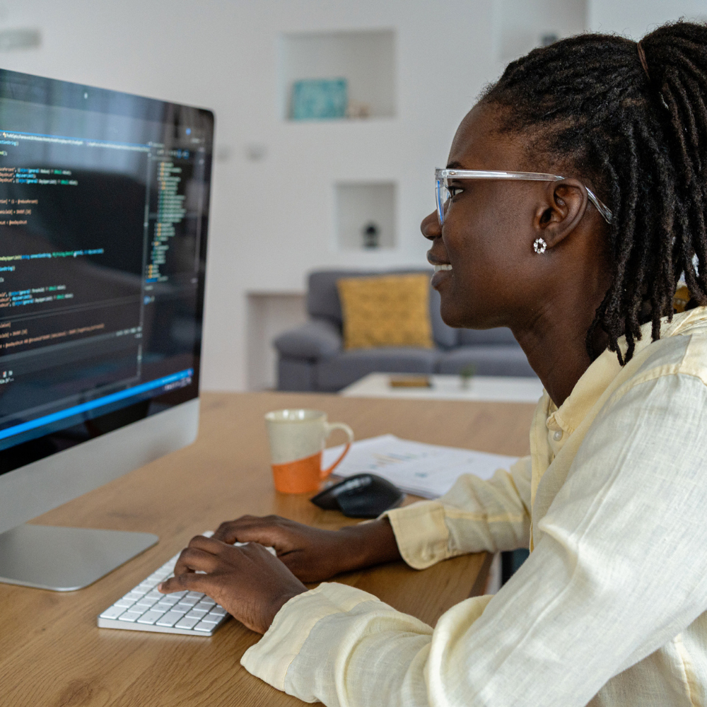 Person wearing glasses types on a keyboard while looking at code displayed on a large computer monitor in a home office setting.