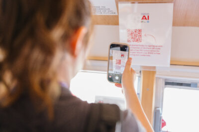 A person scans a QR code on a printed AI-themed sign using their smartphone.