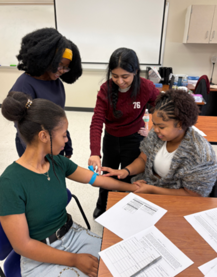 Four scientists in lab coats work in a laboratory; one woman looks through a microscope, while others use digital tablets and examine lab equipment.