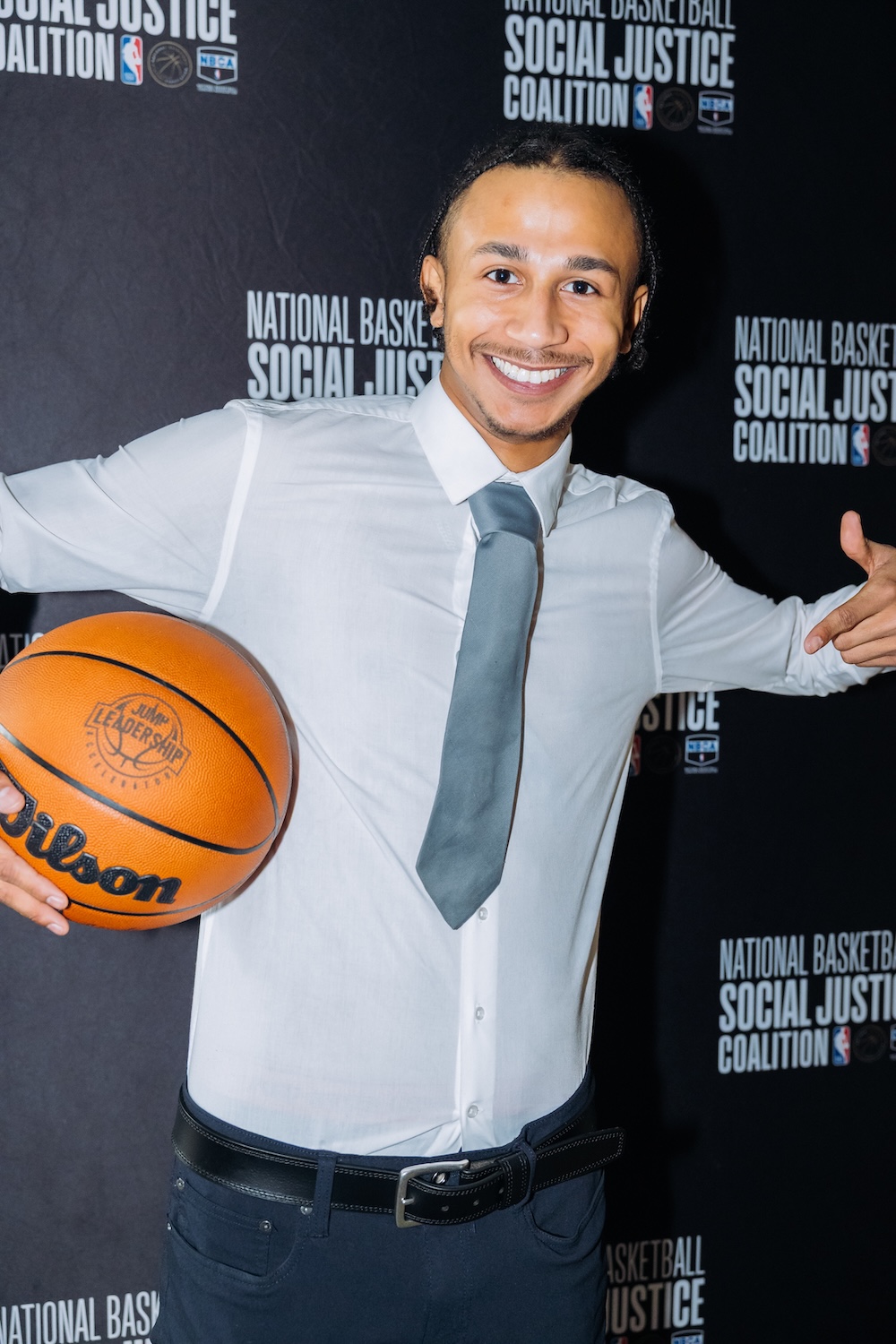 A person in a white shirt and tie smiles while holding a basketball in front of a