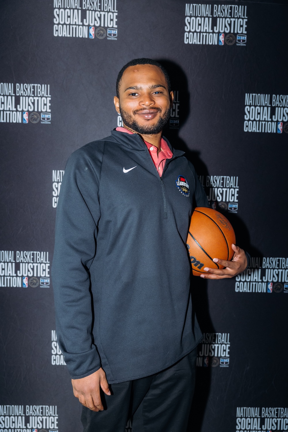 A person in a black jacket holding a basketball stands in front of a