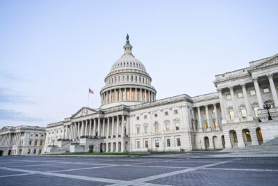The United States Capitol building in Washington, D.C., with the American flag flying and lights on inside, photographed at dusk from the front plaza.