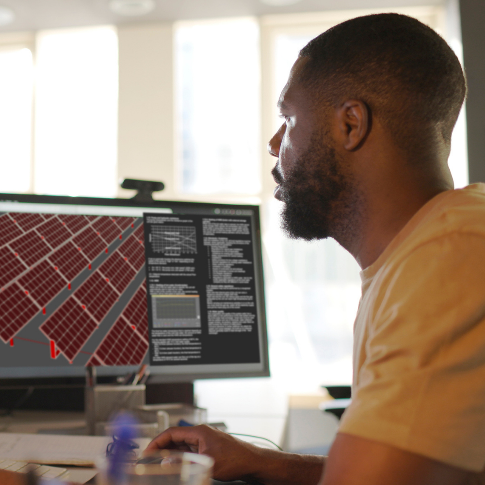 A man sits at a desk, looking at a computer screen displaying a grid-like map and technical data in a modern, sunlit office.