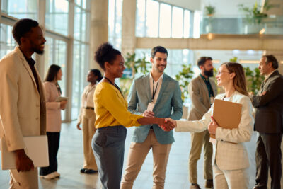 A group of professionals converse and two women shake hands in a bright, modern office lobby.